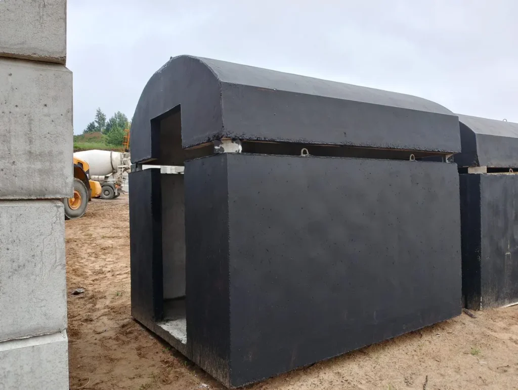 Elementy prefabrykowanej piwniczki betonowej pomalowanej na czarno, z zaokrąglonym dachem, na placu budowy.