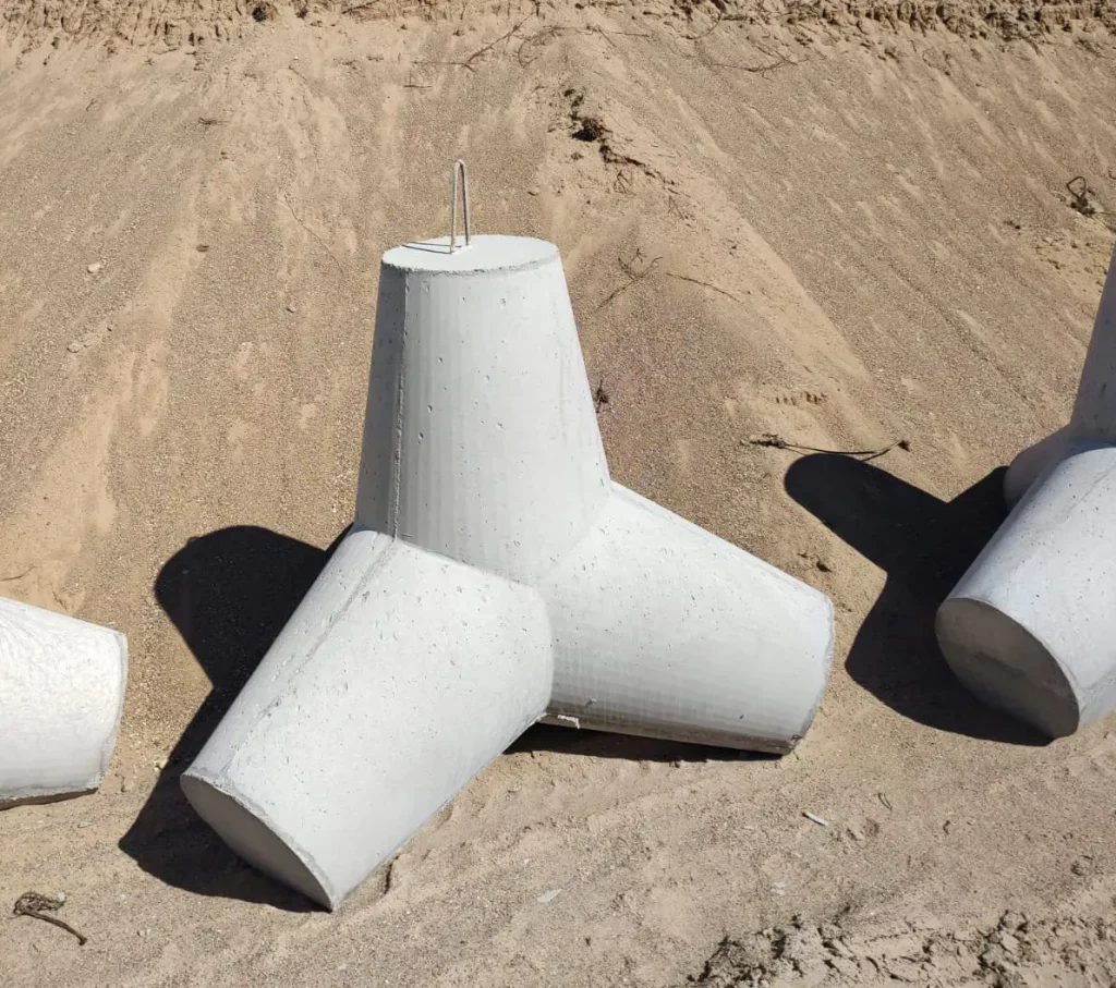Betonowy element w kształcie tetrapodu, służący do ochrony brzegów, leżący na piaszczystym podłożu.