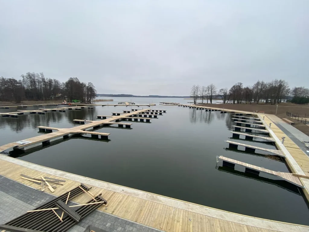 Szeroki widok na nowo wybudowaną marinę lub przystań z rzędami drewnianych pomostów pływających nad spokojną wodą.
