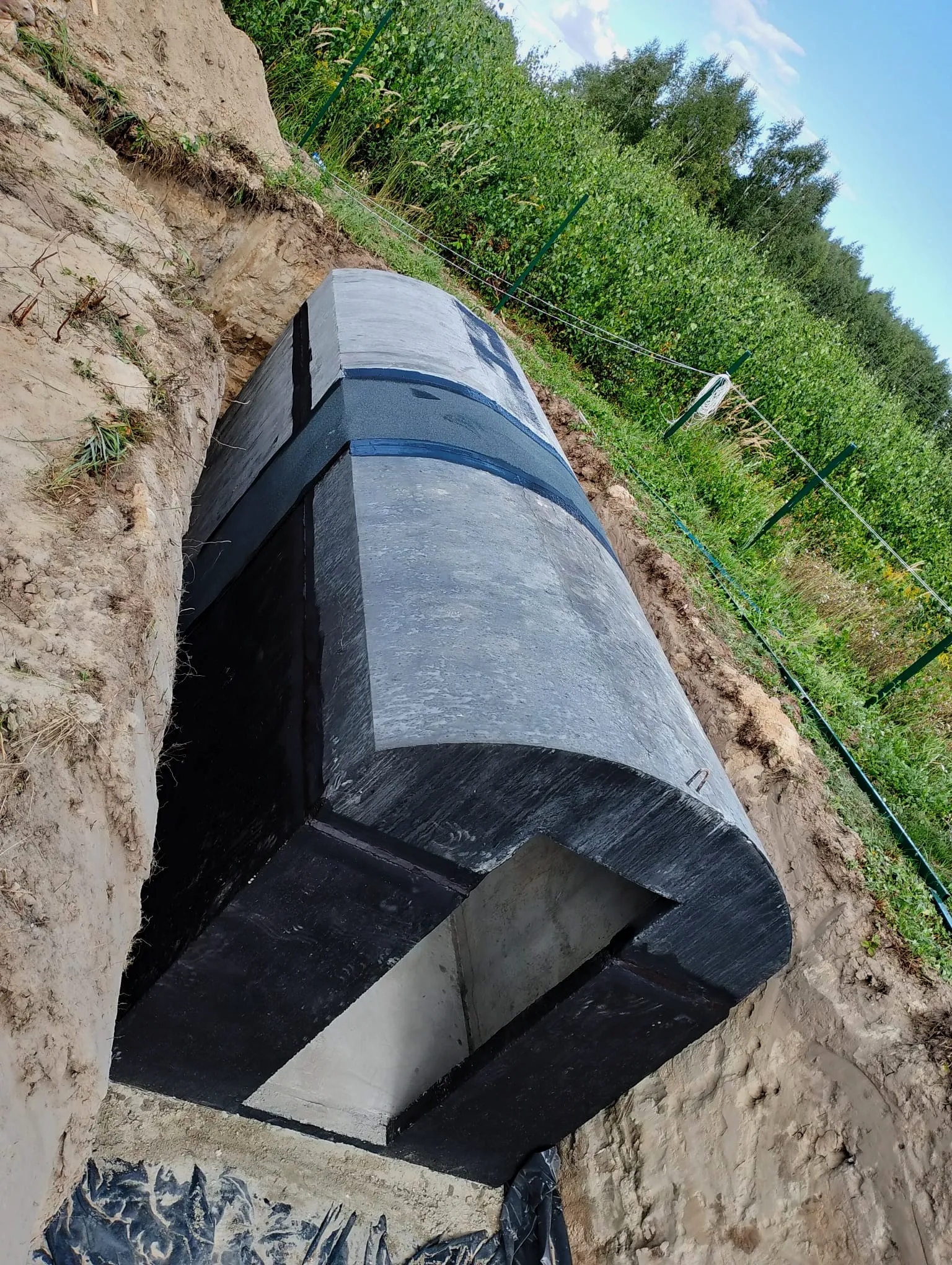 Elementy prefabrykowanej piwniczki betonowej pomalowanej na czarno, z zaokrąglonym dachem, na placu budowy.