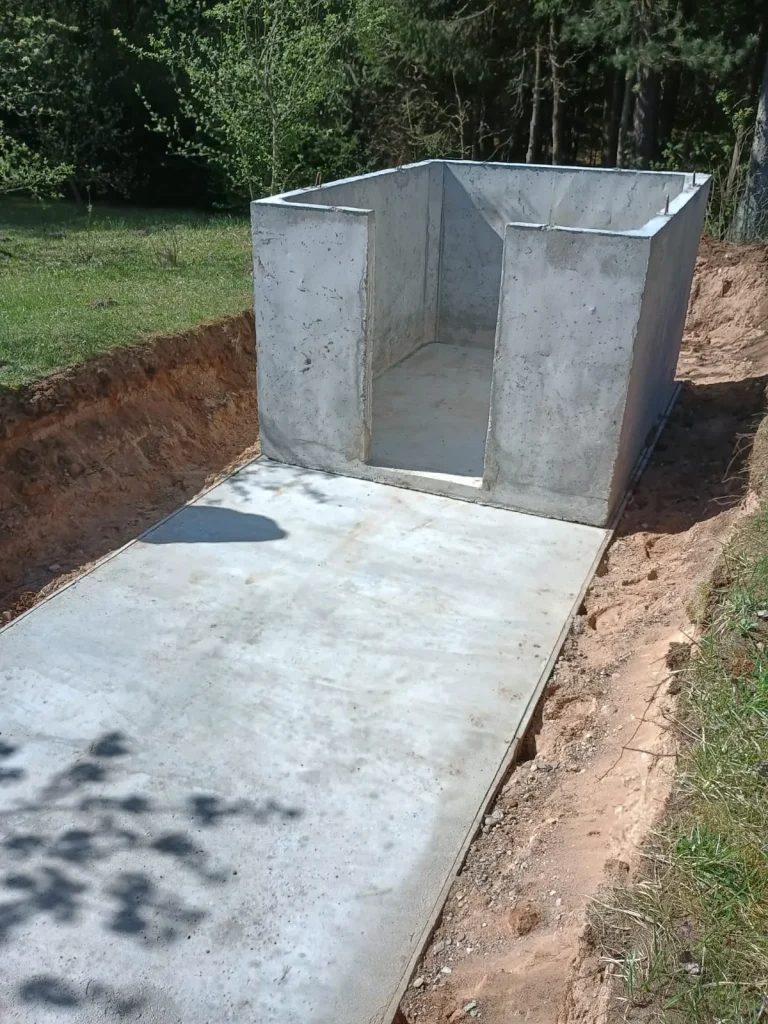 Elementy prefabrykowanej piwniczki betonowej na placu budowy.